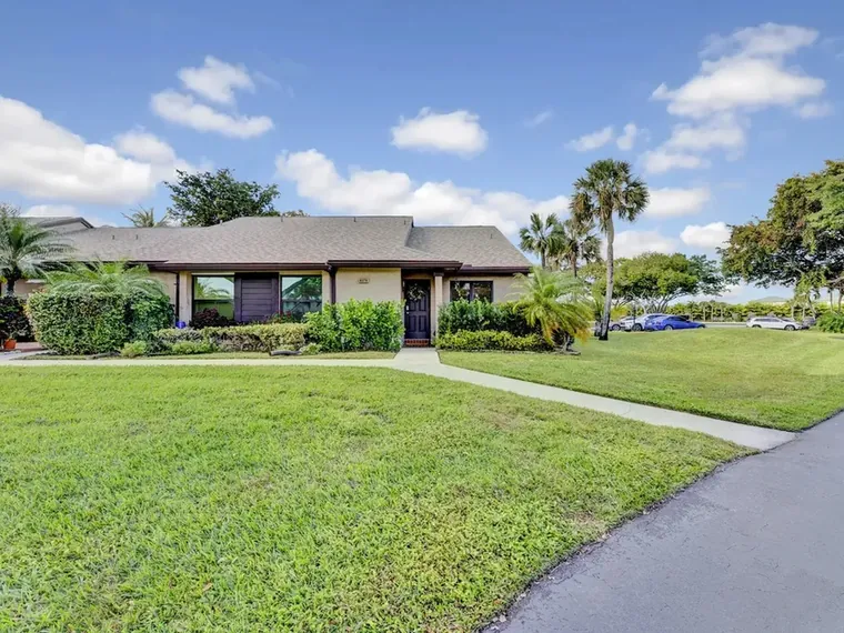 Single-story villa with a wide front lawn, a palm and a dark front door at 8379 Boca Glades Blvd E, Unit 1480, Boca Raton, FL 33434